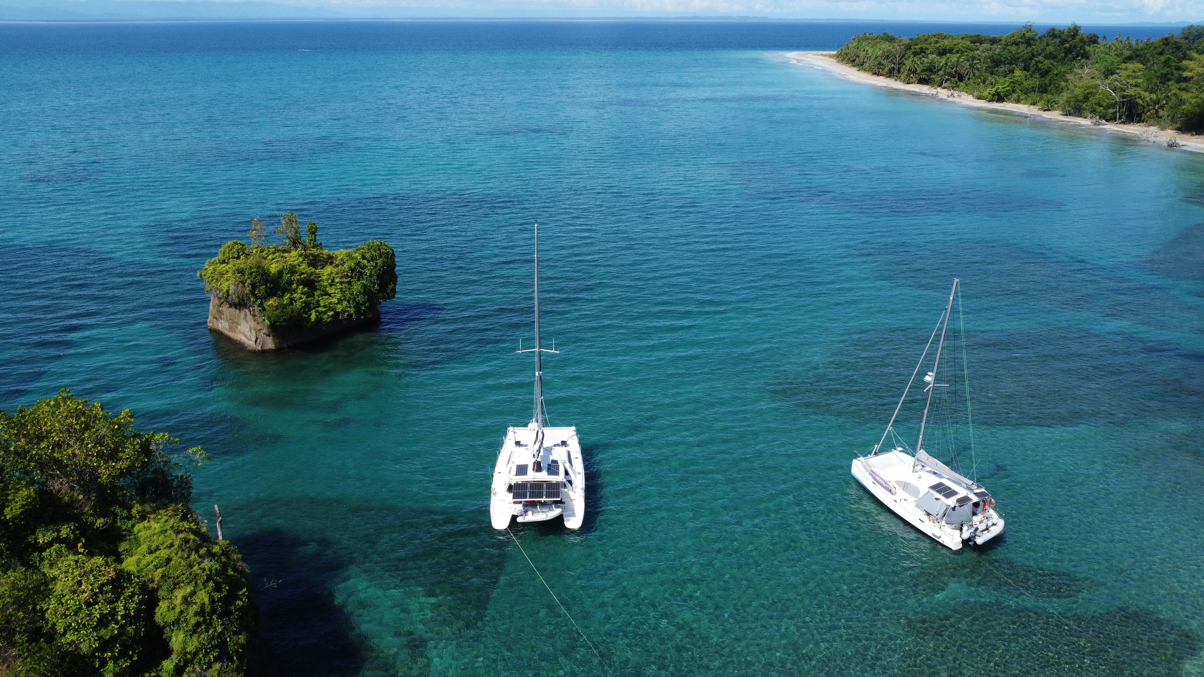 Aerial drone view of Surfnsail's two catamarans, Aventura and Exta Sea, anchored side by side near a small island in Bocas del Toro